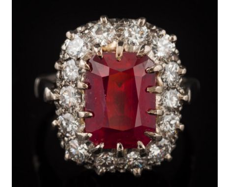 A ruby and diamond oblong cluster ring: with central oblong ruby 11.2mm long x 8.1mm wide, claw-set within a surround of bril