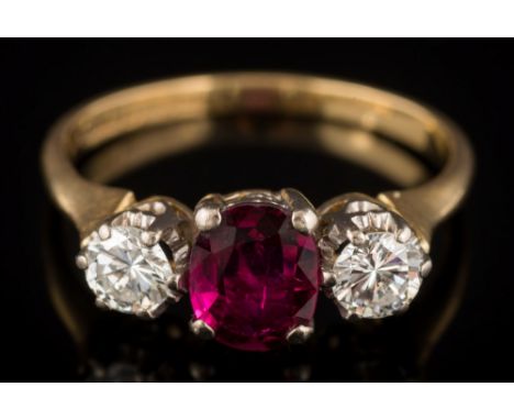 An 18ct gold ruby and diamond three-stone ring: with central oval ruby 6.9mm x 5.3mm estimated to weigh 0.65ct between circul