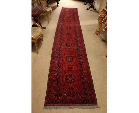 A very long burgundy ground Afghan Runner, a row of varied medallions inside a conforming border, 488cms x 83cms (192" x 32 1