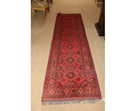 A burgundy ground Afghan Runner, with a centre row of varied medallions inside conforming borders, 302cms x 84cms (119" x 33"