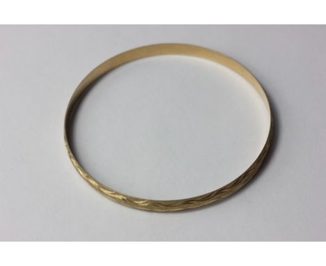 A 9ct gold bangle with engraved and textured decoration