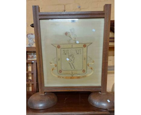 An antique oak framed fire screen with silkwork armorial under glass panel, set on massive semi-circular bases
