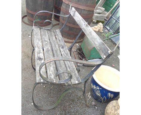 A teak garden bench with slatted seat, set on wrought iron scroll ends