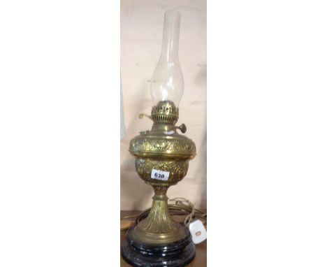 An old oil lamp with an embossed brass reservoir, set on black ceramic base, with Duplex burner and glass chimney
