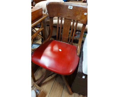 A vintage oak framed swivel office chair with red vinyl upholstered seat, set on a four star base