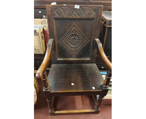 An antique oak wainscot chair with carved panel back, open armrests and solid seat, set on turned front supports