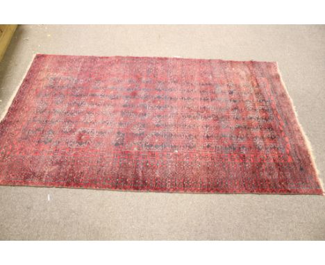 A 20th century rug. The carpet has a red ground decorated with a geometric pattern, 116cm x 202cm