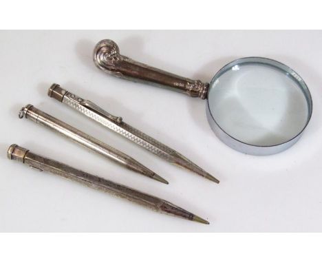 Three various silver cased propelling pencils, of shaped outline with articulated centres, 12cm wide, and a magnifying glass 