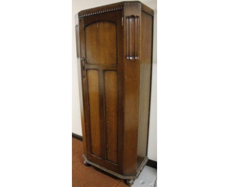 An early 20thC oak hall wardrobe, with canted front and panel door, hinging to reveal a single shelf on compressed bun feet, 