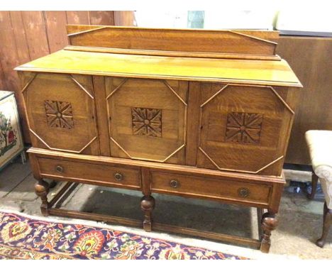 A 1930s/40s oak sideboard with ledge back above a rectangular moulded top over three panel doors with central foliate motifs 