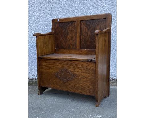 A small oak hall seat, the panel back with stylised floral carving over a hinged seat, raised on panel end supports (91cm x 7