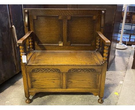 An oak monk's bench, c.1930, the panelled folding top over open arms with bobbin turned supports, above a hinged seat reveali