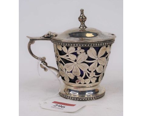 An Edwardian silver mustard of pierced cylindrical form, having a hinged lid surmounted by a finial, with blue glass liner, C