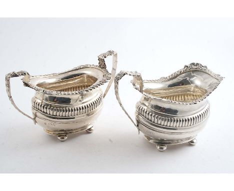 AN EDWARDIAN MATCHING CREAM JUG & MATCHING SUGAR BASIN with foliate shell & gadrooned rims, part-fluted bodies & button feet,