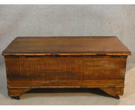 A 19th century pine trunk with hinged lidded top and iron carrying handles on shaped and moulded bracket feet on brass caster