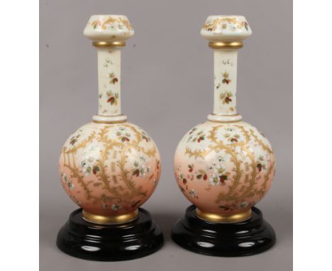 A pair of 19th century blush glass bottle vases with applied enamel and gilt decoration raised on black glass plinth.