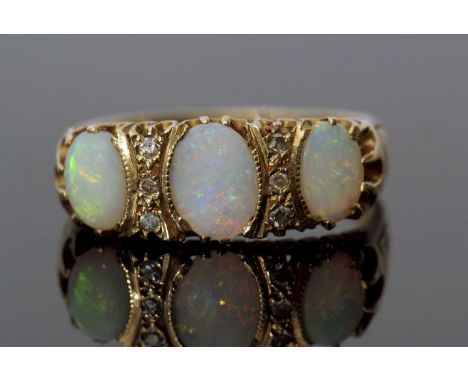 Three stone opal and diamond ring featuring three graduated oval shaped opals, highlighted between by two rows of small diamo