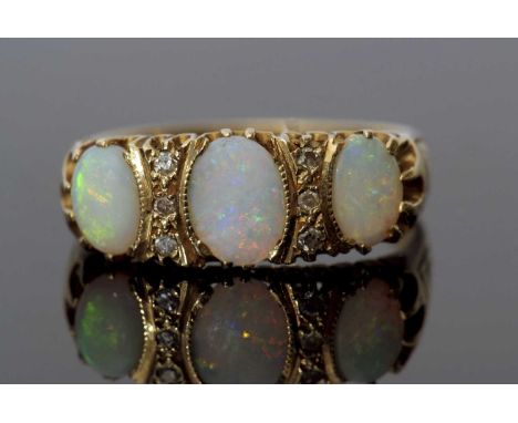 Three stone opal and diamond ring featuring three graduated oval shaped opals, highlighted between by two rows of small diamo