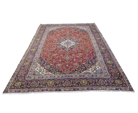 Iranian wool floor rug decorated with a large central red and blue panel with stylised floral detail surrounded by a blue flo