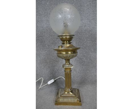 A converted Victorian brass oil lamp with fristed globe shade. The lamp has a fluted column design on a square repousse base.