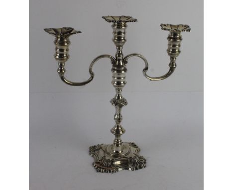 A modern silver two branch, three light candelabraWith a knopped stem, on a raised square base with shell corners, spool shap