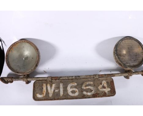 Pair of vintage vehicle headlights, mounted on a bar, with registration plate. 
