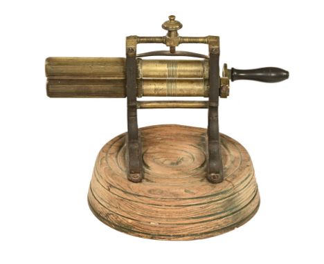 A large 19th century brass and iron crimping tool, raised on a circular wooden base.  Height 30 cm, maximum width 35 cm.