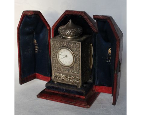 A late Victorian silver carriage clock, with a pointed ogee top above a rectangular body decorated with scrolling leaves and 