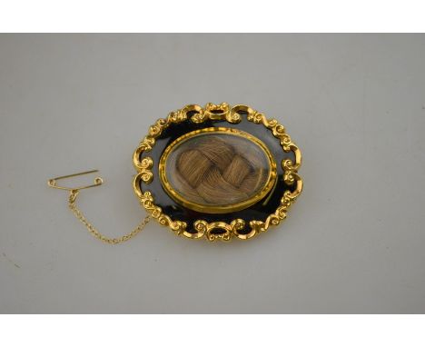 An oval mourning brooch having central hairwork with black enamel surround in gold scrollwork frame Condition Report Showing 