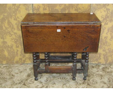 A small antique oak drop leaf gateleg table with frieze drawer raised on turned bobbin and block supports united by stretcher