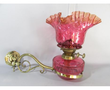 A Victorian brass wall bracketed oil lamp with a crimped Cranberry glass shade and font. 