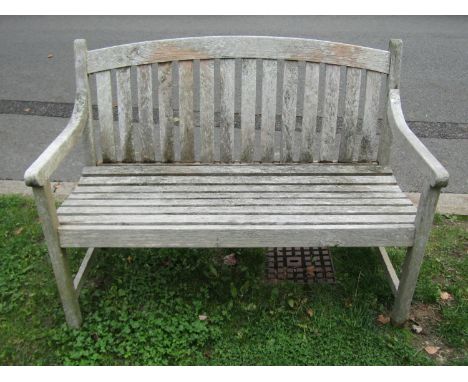 A weathered teak two seat garden bench with slatted seat and back beneath an arched rail, 120 cm wide