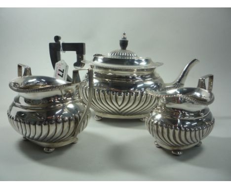 A SILVER THREE PIECE TEA SERVICE, with half embossed reeded design, teapot with ebonised handle and finial, all set on squat 