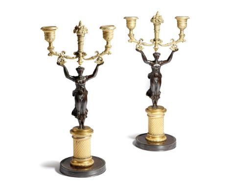 A pair early 19th century French gilt and patinated bronze figural twin-light candlesticks, each modelled with a classical ma