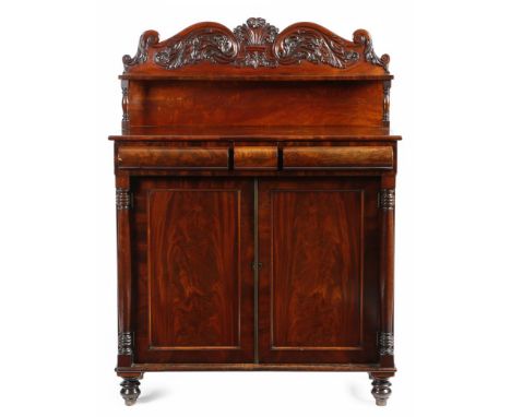 A William IV mahogany chiffonier, the raised back carved with scrolls and leaves, with a shelf on turned supports, above a pa