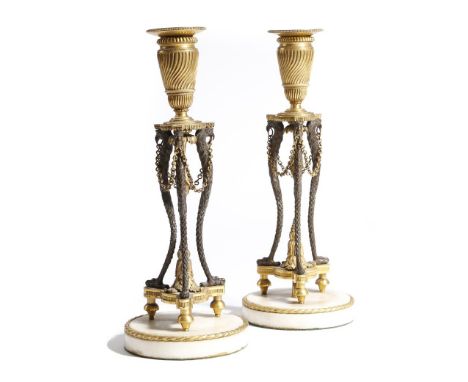 A pair of early 19th century gilt and patinated bronze candlesticks, each with a detachable drip-pan above a spiral fluted ur