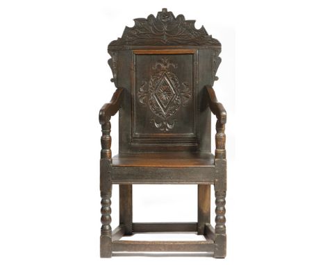A late 17th century oak panelled back open armchair, the surmount carved with leaves, above a lozenge panel, with scroll arms