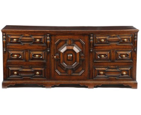 A late 17th century oak dresser, the boarded top above a geometric panelled cupboard door enclosing a shelf, flanked by three