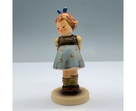 Hand-painted porcelain features a little girl in brown and blue dress holding her hands. Goebel backstamp. Hummel-Hummel impr