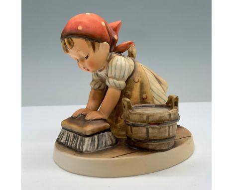 Hand painted figure of a girl in a headscarf and apron kneeing down scrubbing the floor with a cleaning brush. A bucket of so