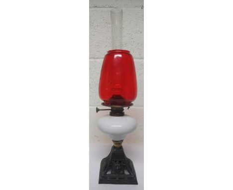 Victorian cast iron oil lamp with a glass reservoir, together with a chimney and a red shade, 52cm high