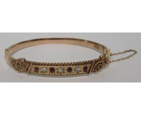 An early 20th century unmarked bi-coloured gold (tested) diamond and ruby bangle, set with three single cut diamonds alternat