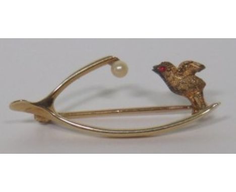 A marked 15ct gold wishbone brooch set with a seed pearl to one end, and a carved bird with pink paste eye at the other end, 
