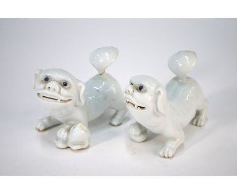 A pair of Chinese ceramic Buddhist guardian lions, white glazed with black eyes, each modelled in a crouching position with a