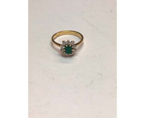 An 18ct yellow gold cluster ring, the central rectangular step-cut emerald surrounded by ten claw set brilliant cut diamonds,