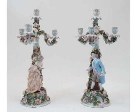 A pair of Sitzendorf figural four-light candelabra, blue underglaze marks, each modelled with a floral encrusted tree-trunk s