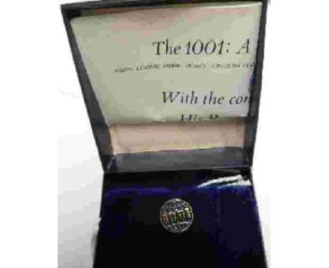 A lapel pin for The 1001: A Nature Trust, depicting a globe in gilt relief with blue enamel and 1001 in gilt relief across th