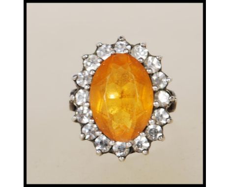 A stamped 9ct gold and silver ladies dress ring set with an oval cut orange stone with a halo of white stones, the shank yell