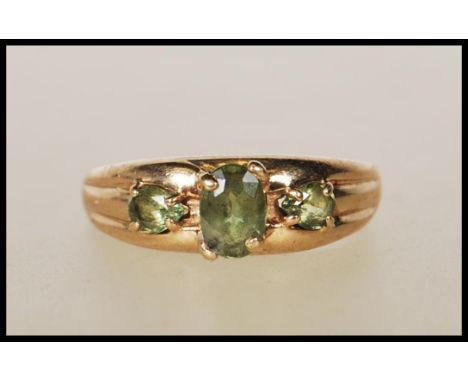 A hallmarked 9ct gold ring with central oval cut green stone flanked by two teardrop green stones on a tapering mount. Hallma