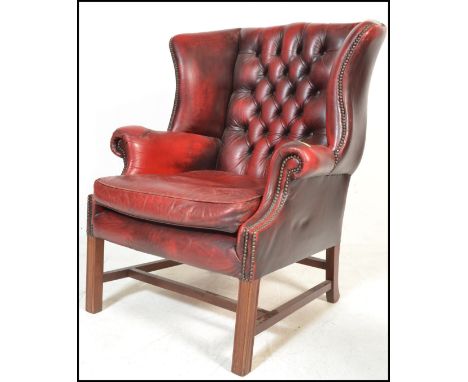 A 20th Century Antique style red leather&nbsp;oxblood Chesterfield wingback armchair raised on straight supports united by st